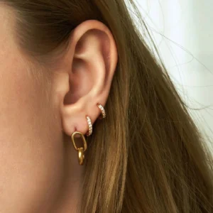 Multiple 18K gold huggie earrings on model ear, mixed sizes showcasing versatility and wearability on real ear