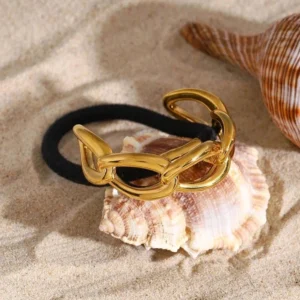 18K gold infinity chain hair cuff overhead view on beach sand with seashells showcasing polished chunky gold chain and black elastic base