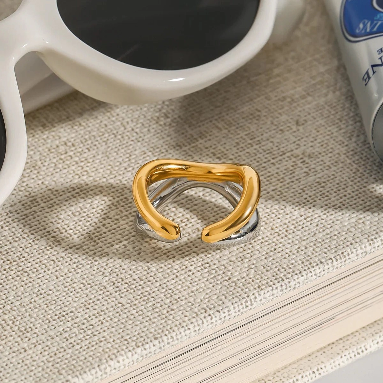 Dual-tone gold and silver intertwined ring on fabric book with accessories, luxury lifestyle styling