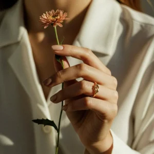 delicate thin twisted 18K gold knot ring on female hand middle finger holding white flower artistic styling