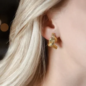 Gold knot earrings worn on ear side view blonde model hypoallergenic stainless steel