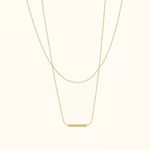 18K Gold Layered Bar Necklace flat lay front view featuring dual staggered chains with polished gold bar pendant