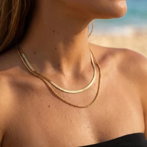 Layered 18K gold chain necklace worn on tanned model at beach - close-up neck view showing mixed chain textures
