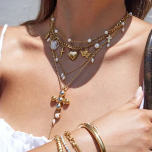 Multi-layer 18K gold necklaces with crystal heart charm and pearl accents styled with gold bracelets on model wrist and neck close-up