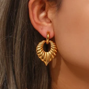 Woman wearing 18K gold leaf drop hoop earrings close-up side view, demonstrating fit and styling on ear, gold-toned hypoallergenic jewelry worn by model