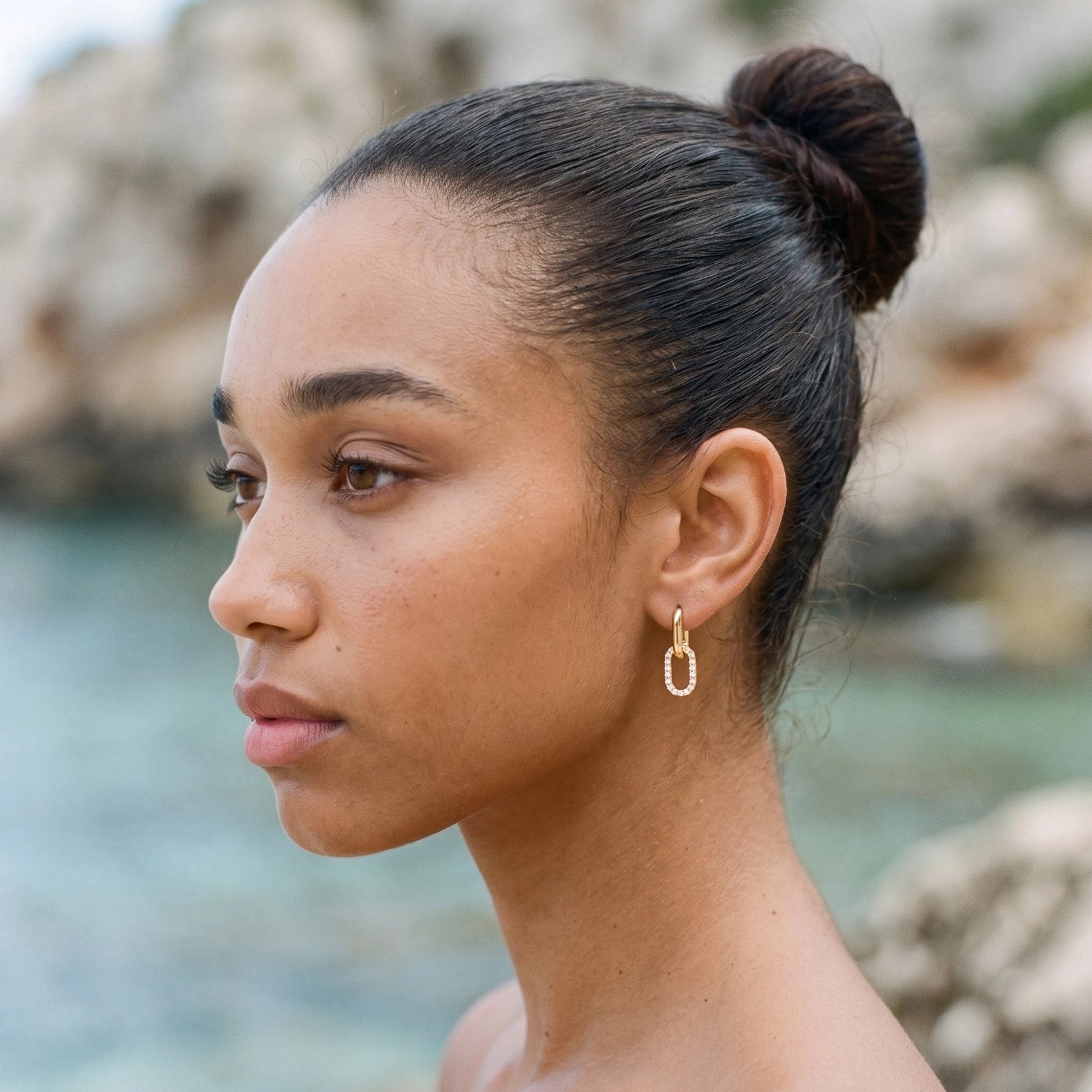 Minimalist 18K gold smooth hoop earring, side outdoor portrait on model at seaside rocky background