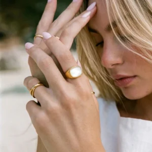 Stackable 18K gold rings with mother-of-pearl signet ring on female hand, close-up wear shot showing delicate gold bands and white pearl stone with pink manicure, outdoor styling