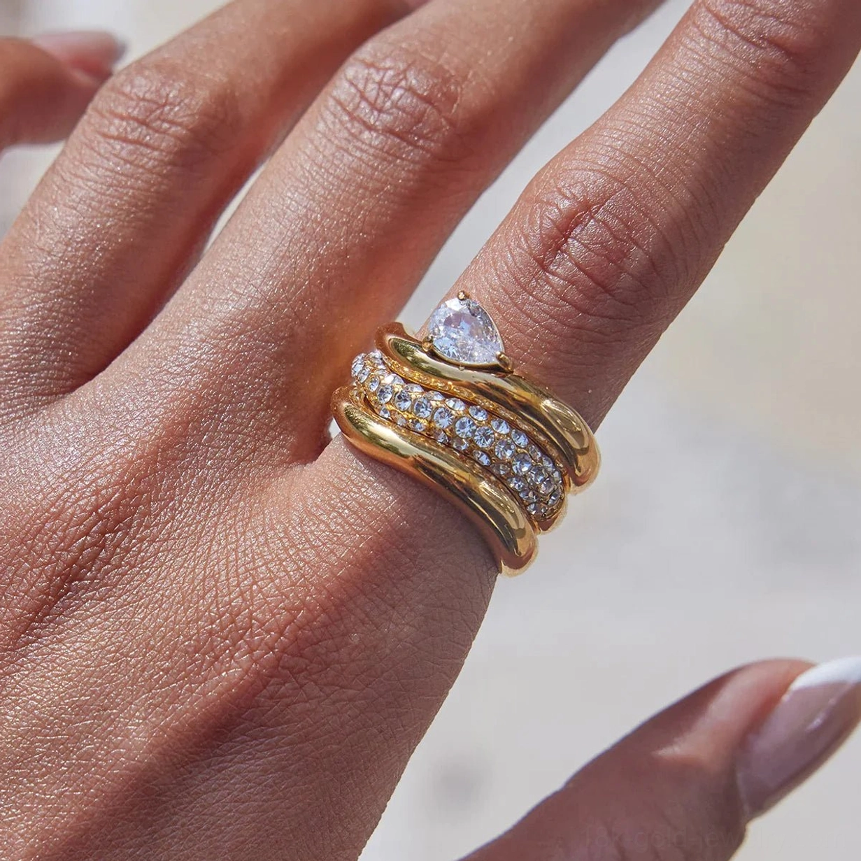 Extreme close-up 18K gold multi-layer twisted ring set with pear-shaped center stone and pavé accent