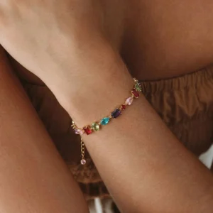 18K gold gemstone bracelet worn on female wrist close-up showing multicolor faceted gems and delicate pearl accent with warm gold finish in studio setting