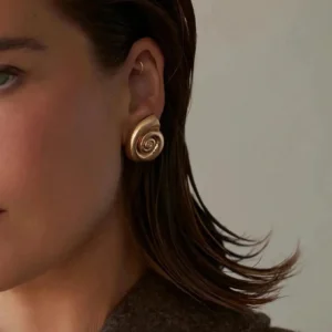 Gold shell earrings worn on model with short dark hair - side ear close-up showing matte gold spiral design