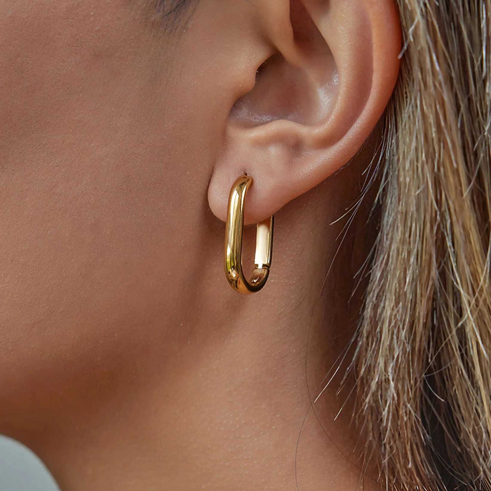 Oval rectangular 24mm gold hoop earrings on ear showing elongated elegant silhouette