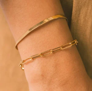Layered 18K gold paperclip arm bracelet and cuff on light-skinned female model upper arm detail