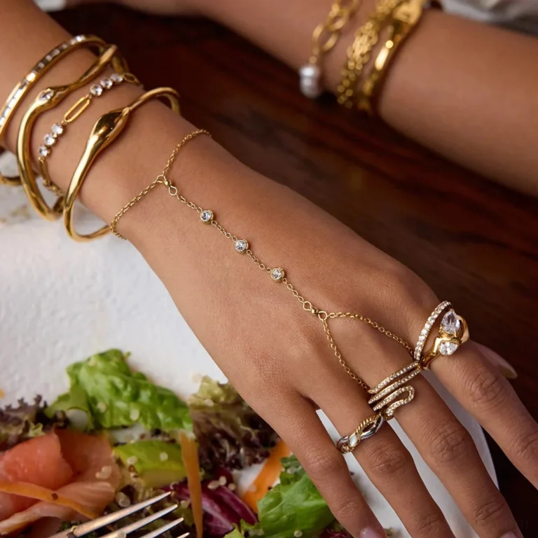 Mixed 18K gold hand jewelry set close-up side view featuring diamond eternity rings paired with layered chain bracelets curved bar bracelets and diamond hand chain on wooden table with salad plate