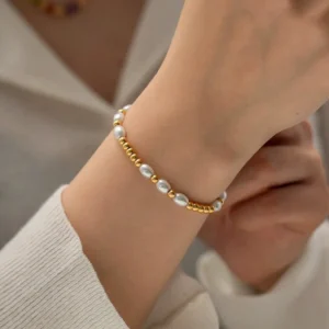 Freshwater pearl and 18k gold bracelet worn on woman's wrist with beige knit sleeve showing real-world everyday wear styling and comfort