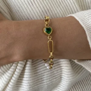 18K gold pearl bracelet worn on wrist with dangling green heart and pearl accents paired with white ribbed sweater for casual elegant styling