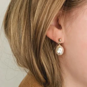 Pearl drop stud earrings worn on model ear close-up showing elegant teardrop shape and gold post design