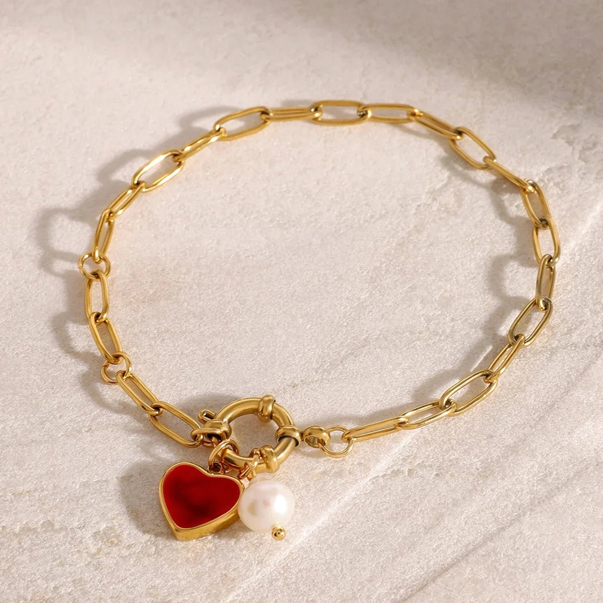 18K gold heart and pearl charm bracelet on marble surface - oblique angle showing dual dangling charms and gold chain links
