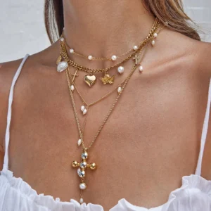 18K gold layered pearl necklace bundle worn on model with white camisole showing stacked charms including cross heart butterfly and pearl accents