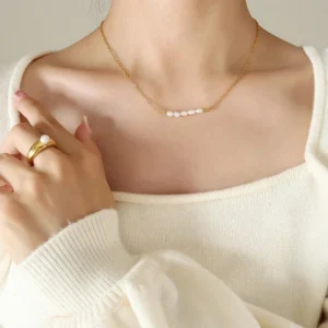 Freshwater pearl gold necklace worn on collarbone, upper body portrait styling with cream square neck knit top and gold ring, delicate dainty chain design