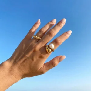 Adjustable 18K gold pearl ring on female hand with blue sky background - side close-up