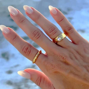 Two stackable 18K gold rings worn on model hand with nude manicure outdoors - pearl ring paired with delicate thin gold band