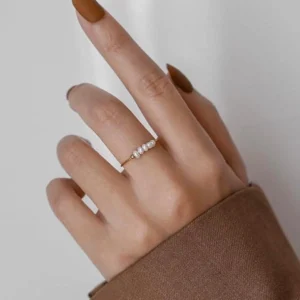 Dainty 18K gold pearl ring worn on female hand with brown nail polish and tailored blazer sleeve