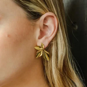 Gold petal stud earrings worn on blonde model's earlobe close-up portrait showcasing shiny polished metallic finish