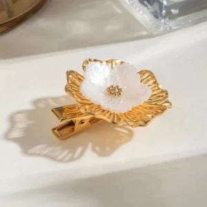 Elegant gold flower hair clip oblique angle shot showing dimensional petal design and pearl detail with soft shadow