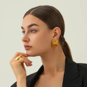 Gold pyramid stud earrings worn on ear close-up profile view on model wearing black blazer