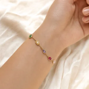 Delicate 18K gold rainbow gem bracelet worn on female wrist close-up side view with silk backdrop