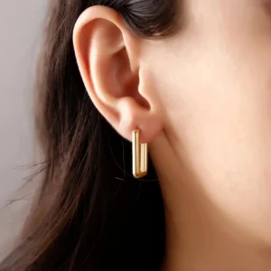 18K gold huggie earrings worn on earlobe close-up showing perfect fit and sleek design on dark-haired model