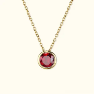 18K gold red birthstone pendant necklace flat lay - bezel-set gemstone on cable chain