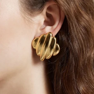 Close-up side view of gold rippled stud earring worn on woman's ear with wavy hair