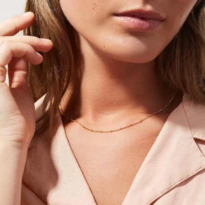 Dainty 18K gold beaded choker necklace worn by woman at collarbone in pink collared top close-up portrait style