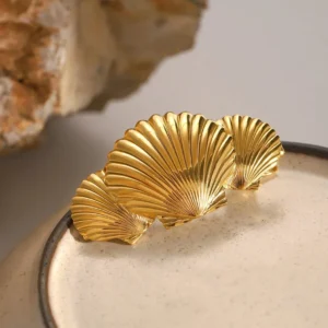 Gold scallop hair clip displayed with decorative ceramic and stone props showing polished gold surface and three-shell design