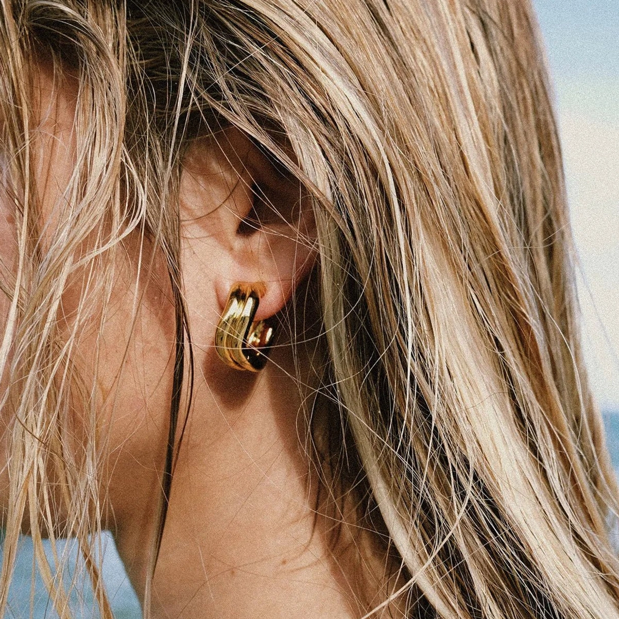 18K gold hoop earrings worn on ear, side profile close-up, blonde model, elegant curvature detail