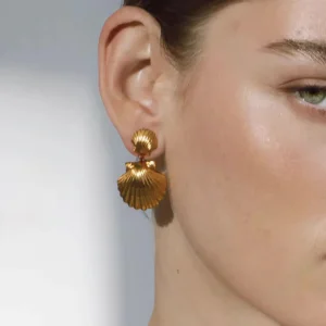 18K gold seashell earrings worn on ear close-up side view displaying warm gold tone striped scallop pendant hanging from earlobe