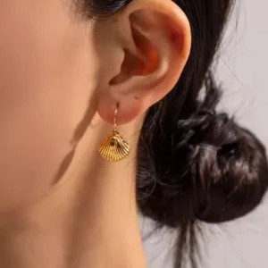18K gold seashell earrings on ear worn by woman, close-up side view showing dangling shell charm in warm golden tone, real wear demonstration