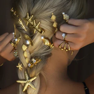 Woman wearing multiple gold ocean-themed hair clips with pearls and gems, blonde braided hair back view close-up, styling inspiration