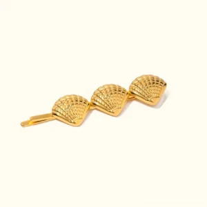 Triple seashell 18k gold hair pin flat lay top view on plain background, displaying embossed shell texture and polished gold metal composition