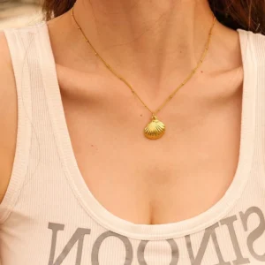 18K gold seashell necklace worn by model at collarbone showing dainty chain styling and coastal pendant design on white background