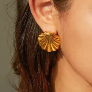 Gold seashell earrings worn on ear, side view close-up of woman modeling the studs, showing fit and shine