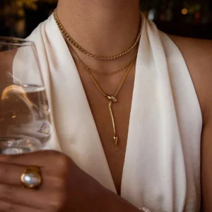 Layered 18K gold necklaces worn on female model, serpent lariat as statement focal piece with mixed gold chain styles, close-up neck shot in elegant dining setting