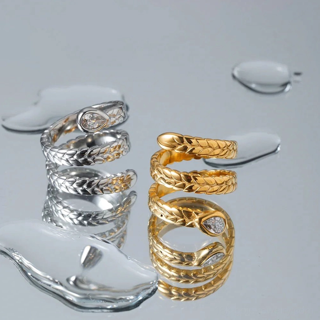 Dual metal 18K gold and silver serpent wrap rings flat lay with water droplet styling props