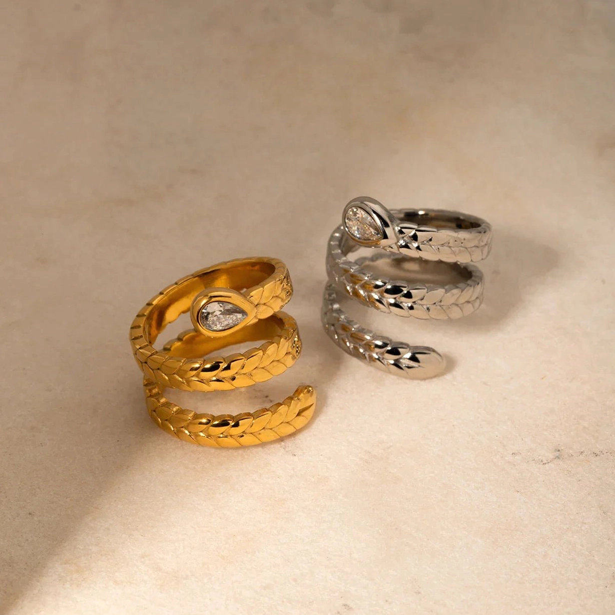 Two-tone gold and silver serpent wrap rings angled flat lay beige background scale texture detail