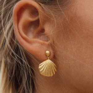 Woman wearing 18K gold shell drop earrings close-up ear view showing textured shell pendant and elegant styling