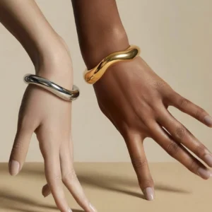 Mixed metal asymmetric cuff bangles on mannequin hands, gold and silver curved open cuffs close-up, dual finish demonstration