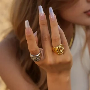 Close-up side view of 18K gold and silver textured signet rings worn on female hand model with manicured nails