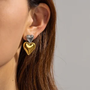 Two-tone heart drop earrings worn on female model's ear, close-up side view showing silver top heart and gold bottom heart design