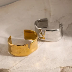 Gold and silver matching open cuff bracelets side by side, top-down angled view on marble surface, comparison of finishes